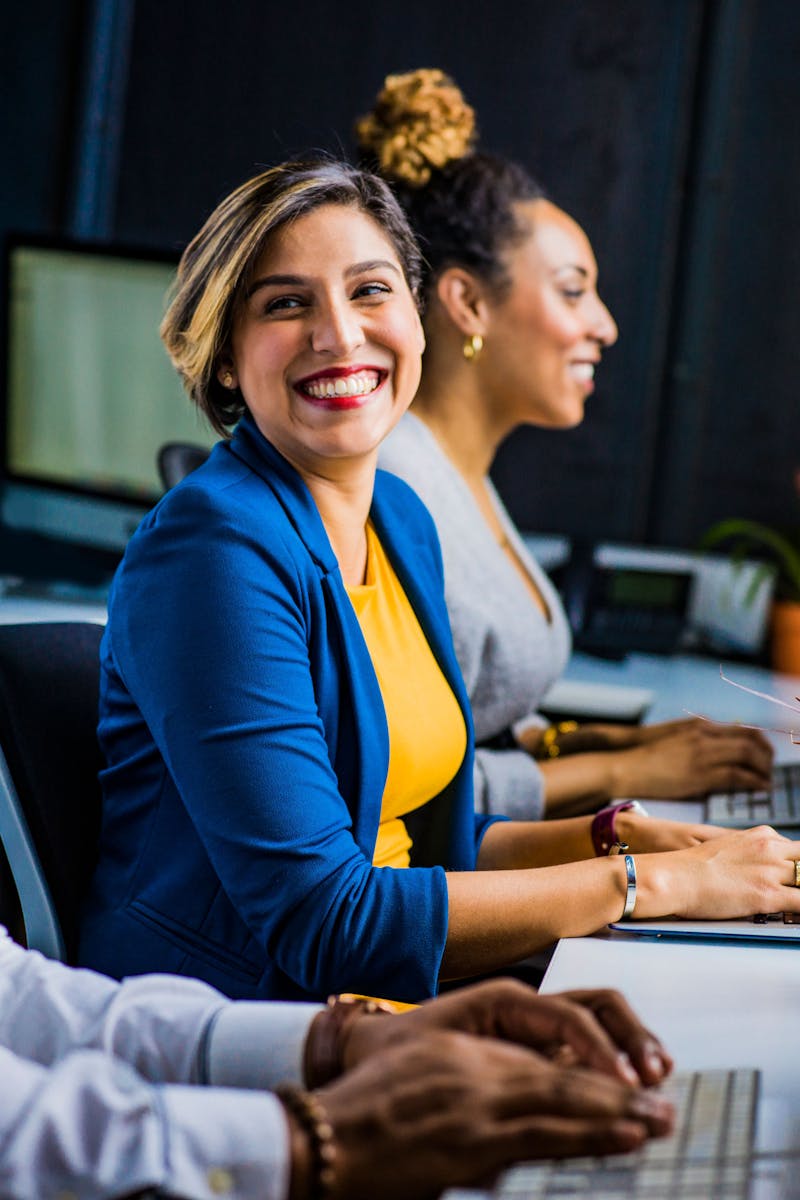 Three diverse professionals working and smiling at office desks, fostering teamwork and collaboration.