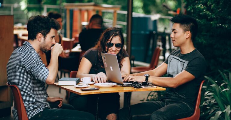 A group of young adults working on a laptop at an outdoor coffee shop, enjoying teamwork and collaboration.